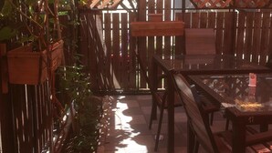 An outdoor patio area with wooden tables and chairs, a lattice fence, and potted plants. - Hotel Bagineti (Mtskheta)