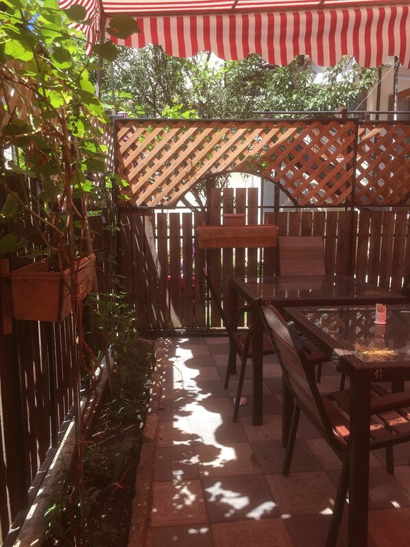 An outdoor patio area with wooden tables and chairs, a lattice fence, and potted plants.