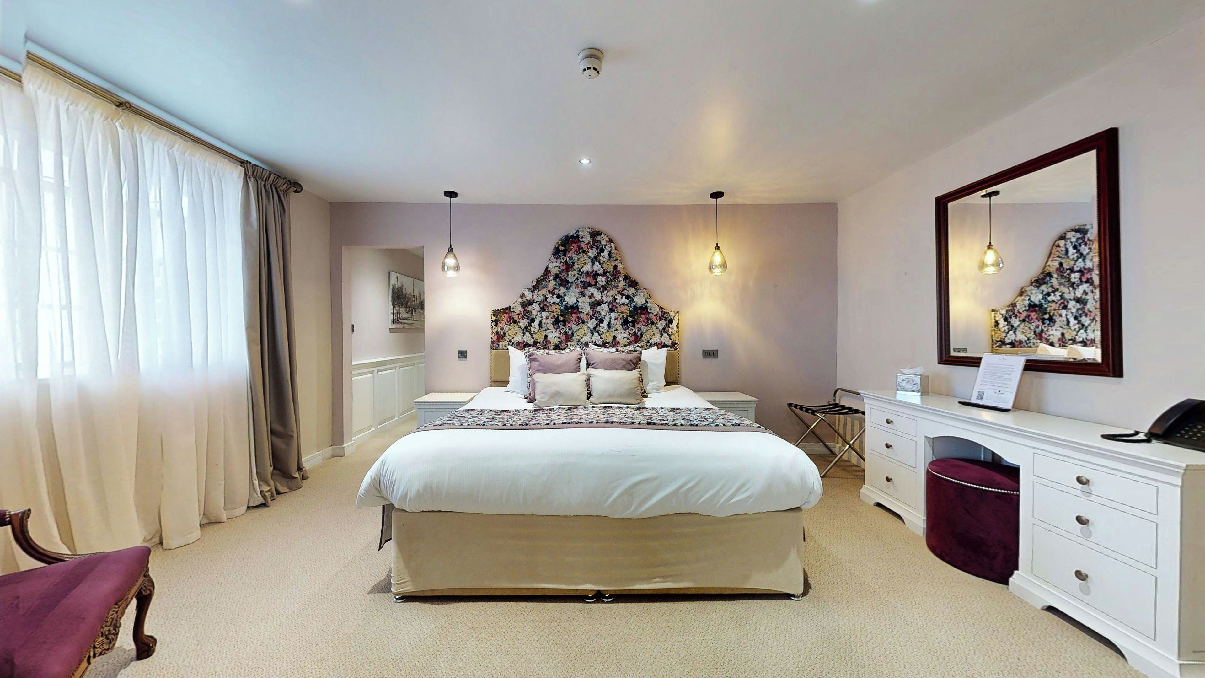 A bedroom with a large bed, bedside tables, a dresser, a mirror, and a window with curtains.
