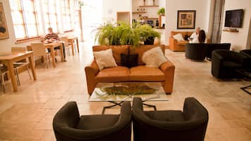 Un vaste espace de vie comprenant un canapé en cuir marron, une table basse en verre et une grande fougère en pot. On y trouve plusieurs options d’assises, notamment un fauteuil noir et une table à manger avec des chaises.