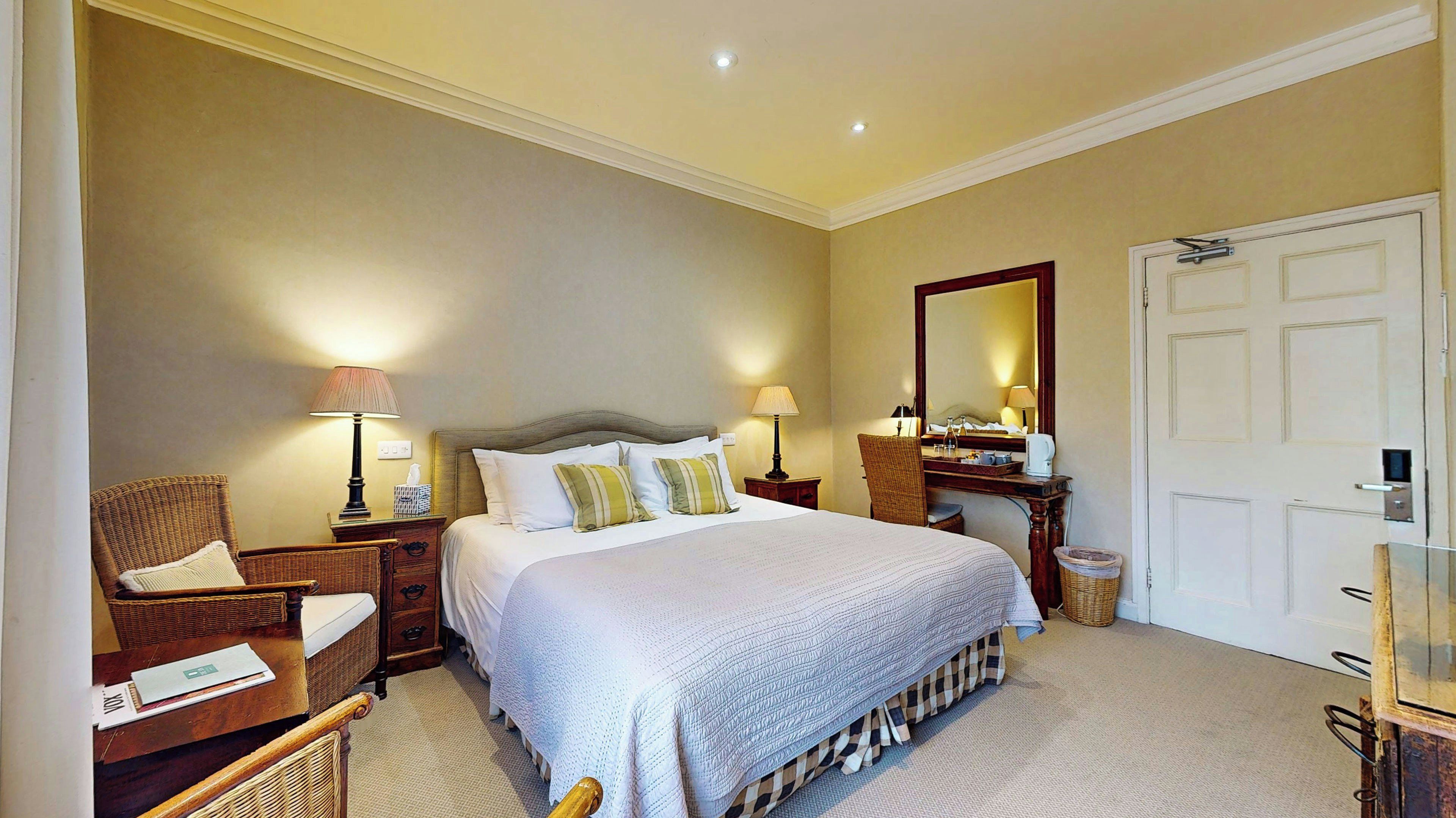 A hotel room with a large bed, two bedside tables, a chair, a desk, a mirror, and a door.