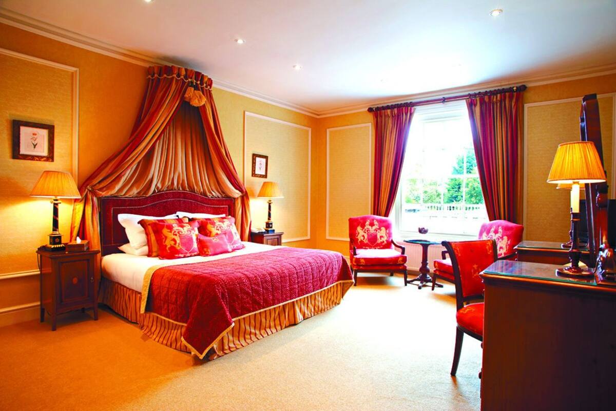 A hotel room with a large bed, two bedside tables with lamps, a desk with a chair, and a window with curtains.