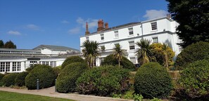 A large, white building with multiple windows and a symmetrical facade, surrounded by well-maintained hedges and trees. - Rowton Hall Hotel and Spa (Chester)