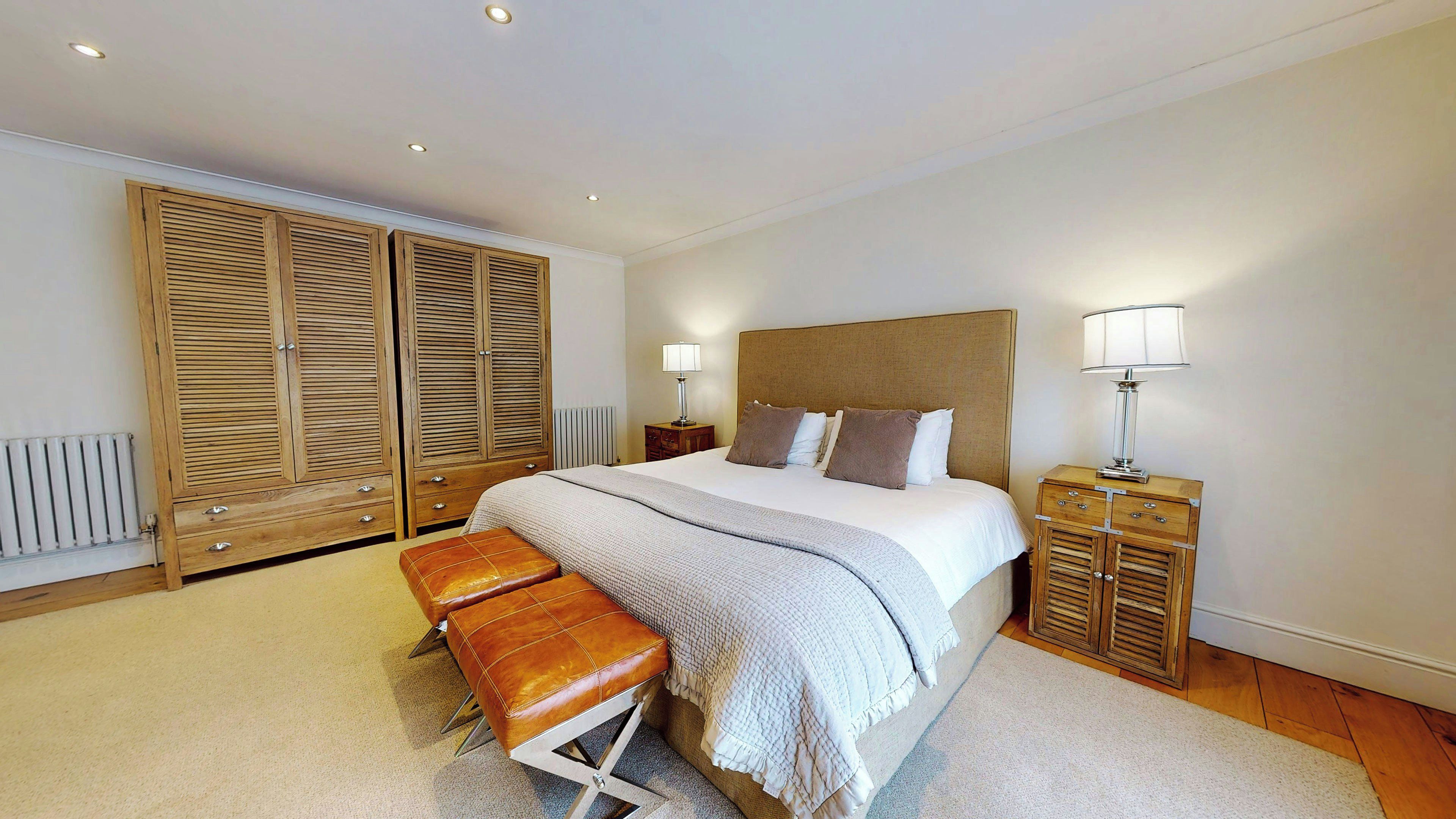 Een slaapkamer met een groot bed, een houten garderobe, twee nachtkastjes en een bankje.