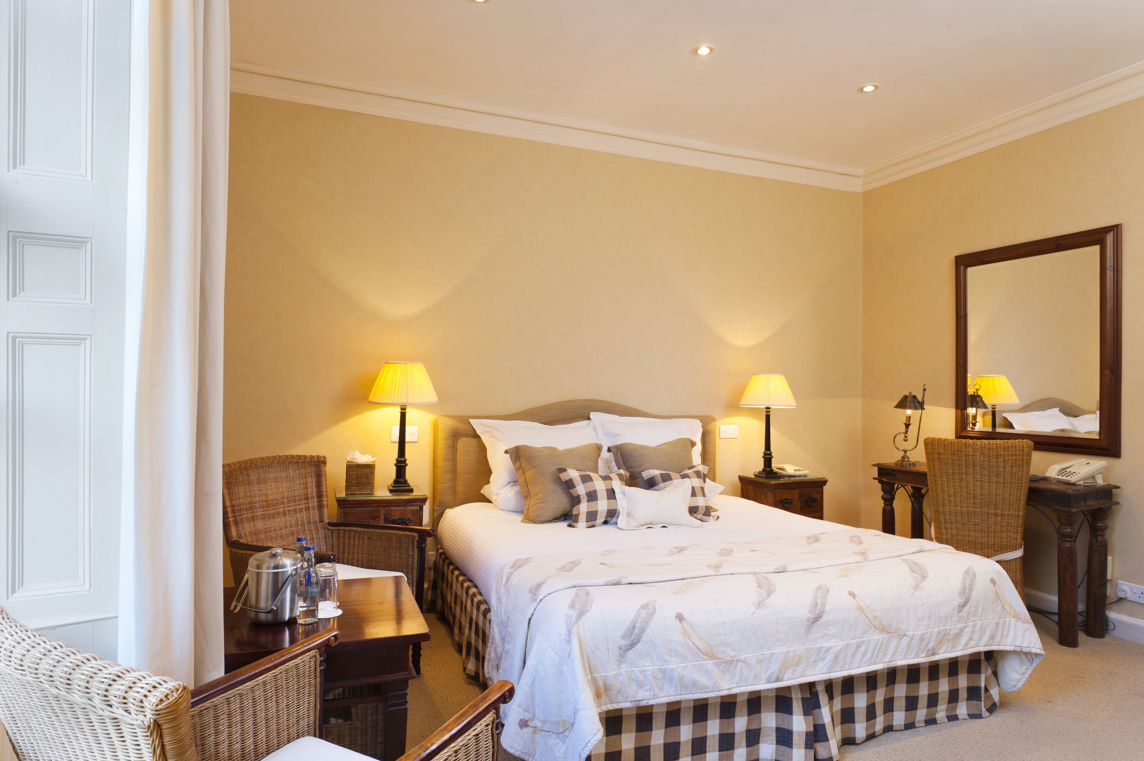 Habitación de hotel con una cama grande, dos mesitas de noche con lámparas, una silla, una pequeña mesa con hervidor y un espejo en la pared.