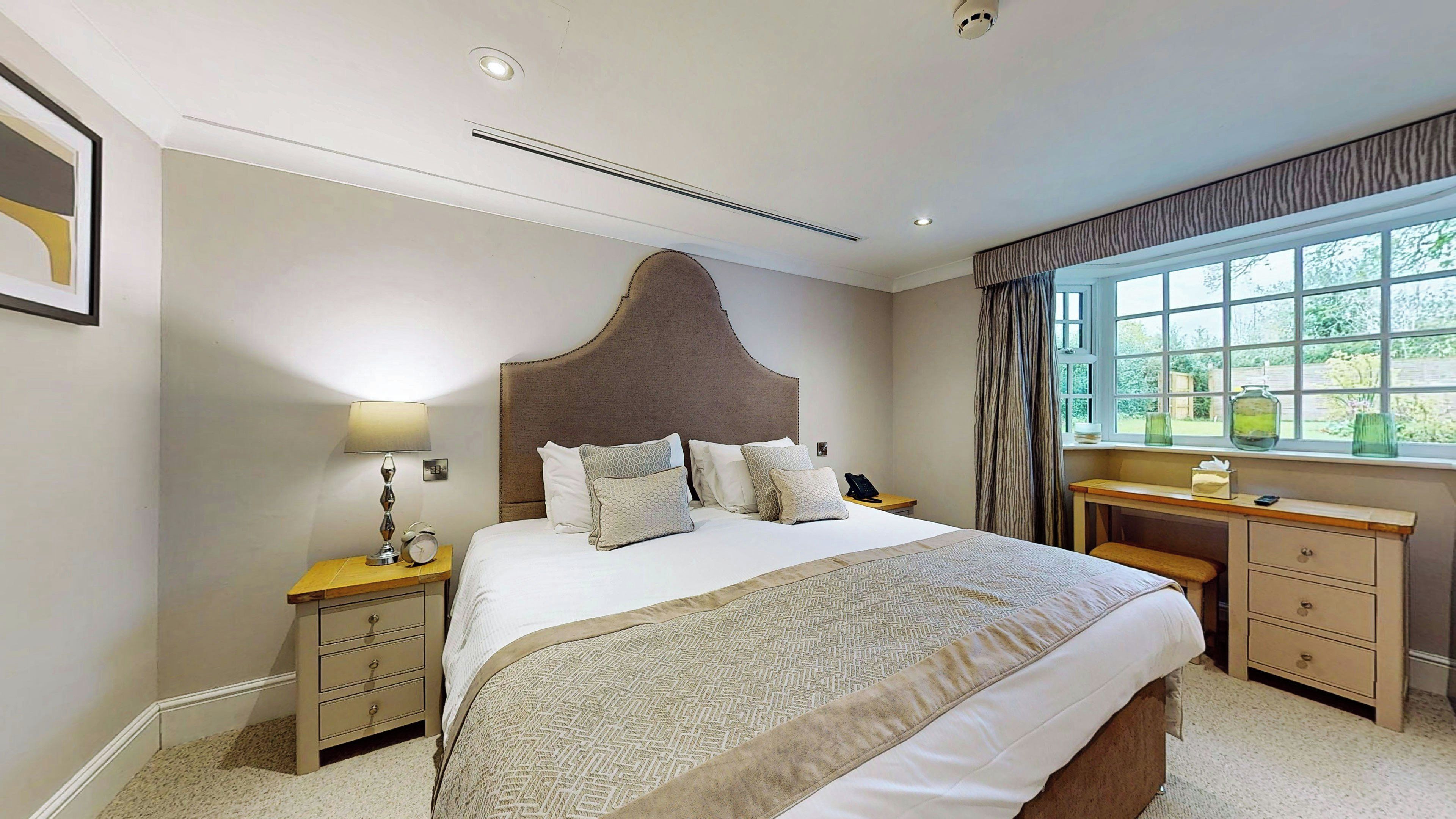 Ein Hotelzimmer mit einem großen Bett, Nachttischen, einem Schreibtisch und einem Fenster mit Vorhängen.
