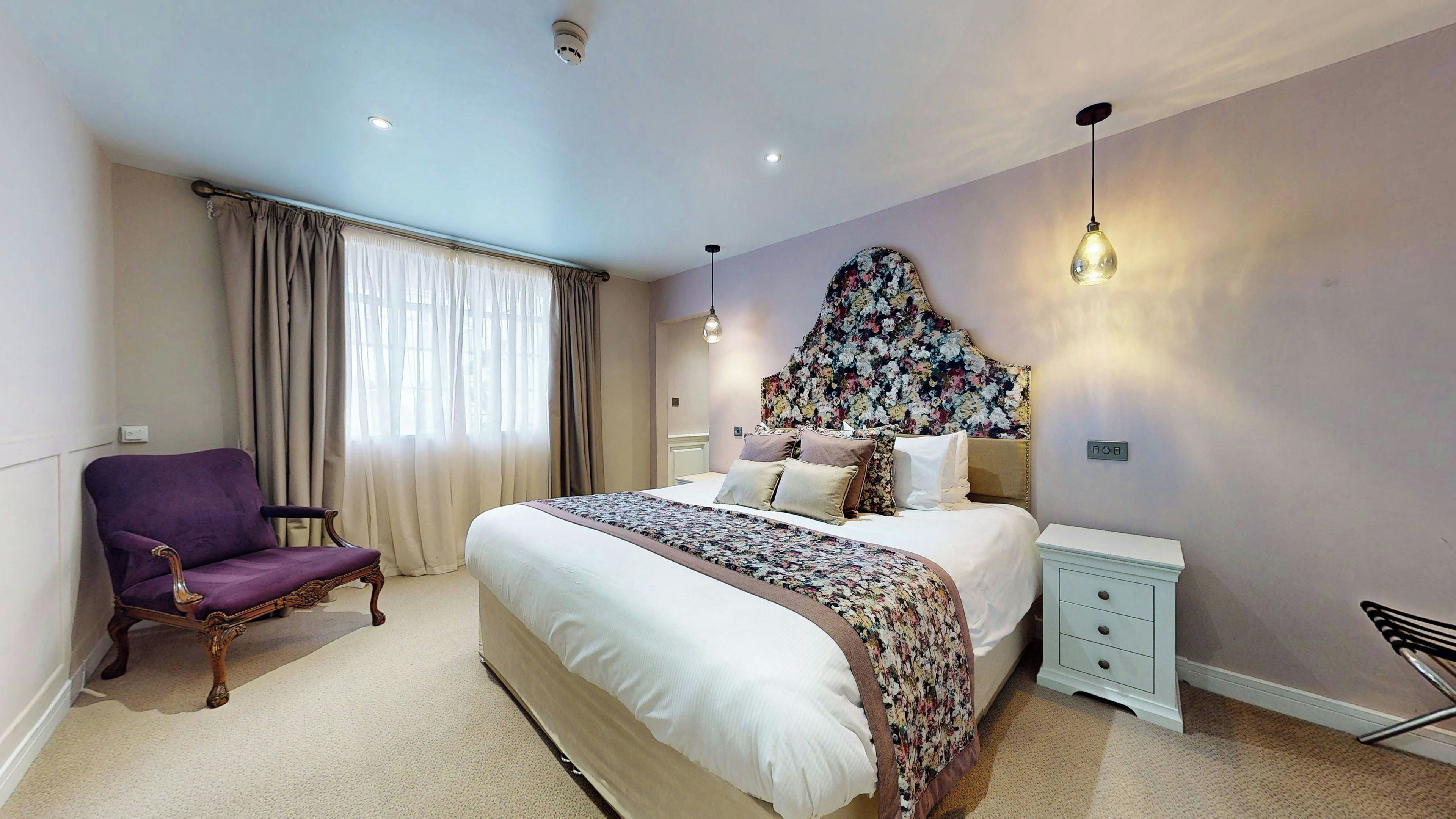 A bedroom with a large bed, a nightstand, a chair, and a decorative headboard.