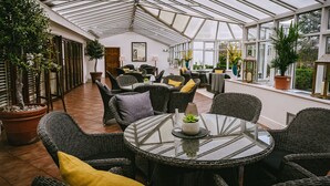 Une véranda meublée de mobilier en osier, agrémentée de plantes en pot et dotée d’une table en verre.