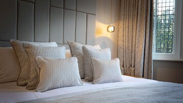 A neatly made bed with multiple pillows and a headboard, a bedside lamp, and a window with curtains.