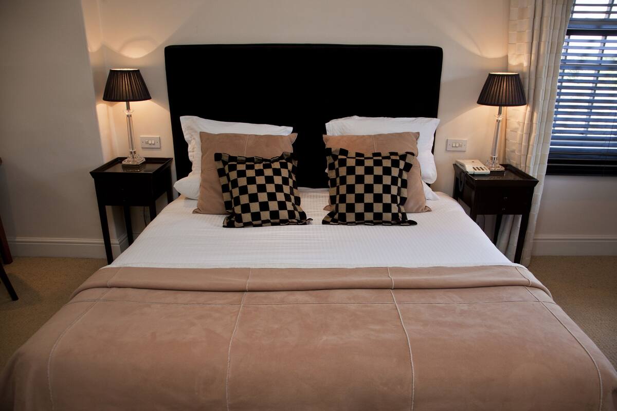 A neatly made bed with checkered pillows, a black headboard, and two bedside lamps on matching nightstands.