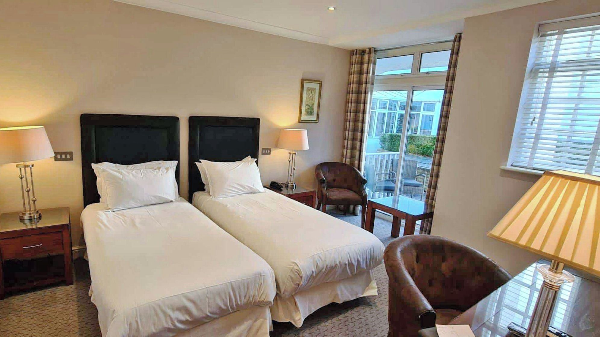 A hotel room with two beds, a chair, a table, and a window with curtains.