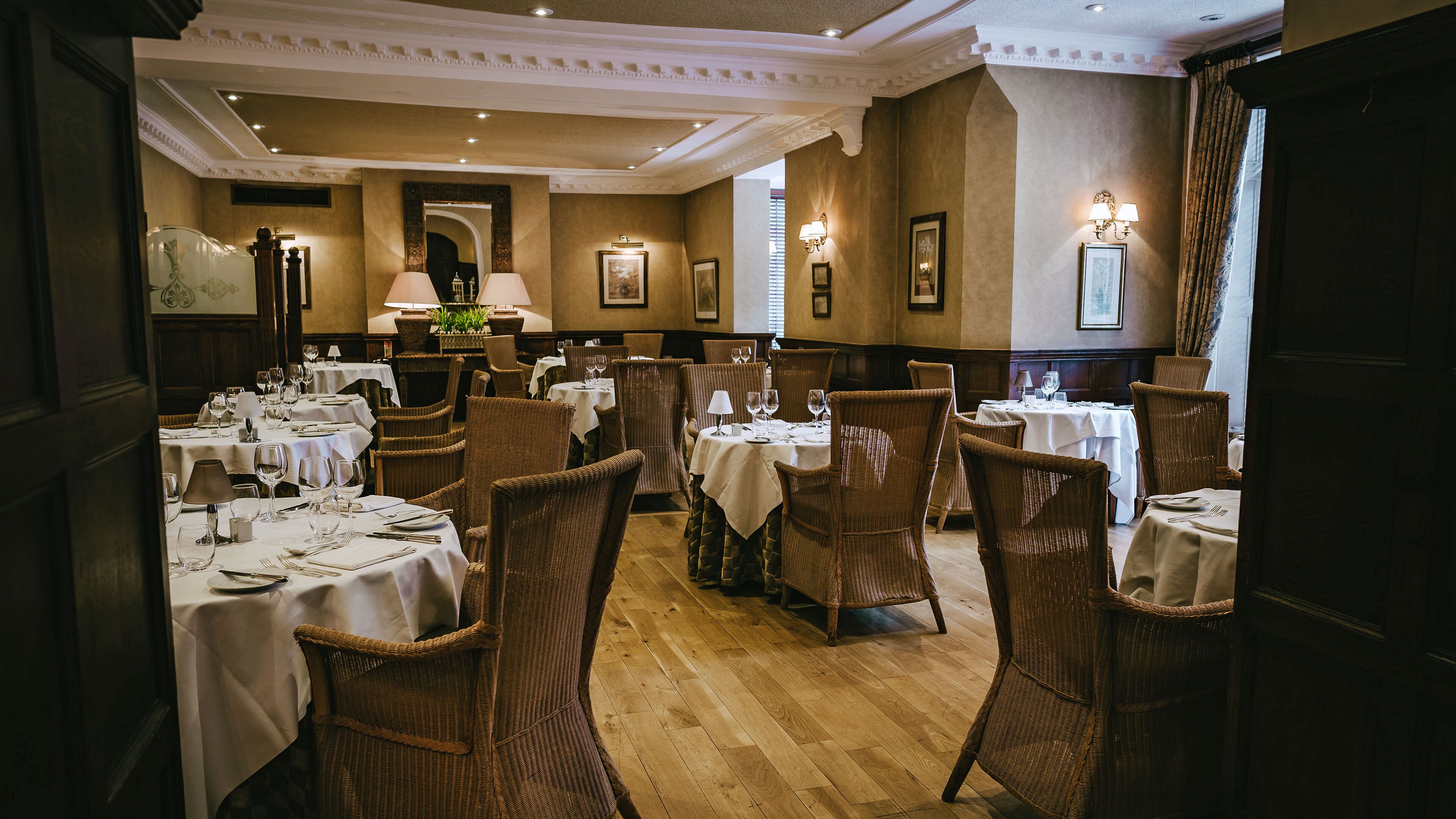 A restaurant with multiple tables set for dining, wicker chairs, and framed artwork on the walls.