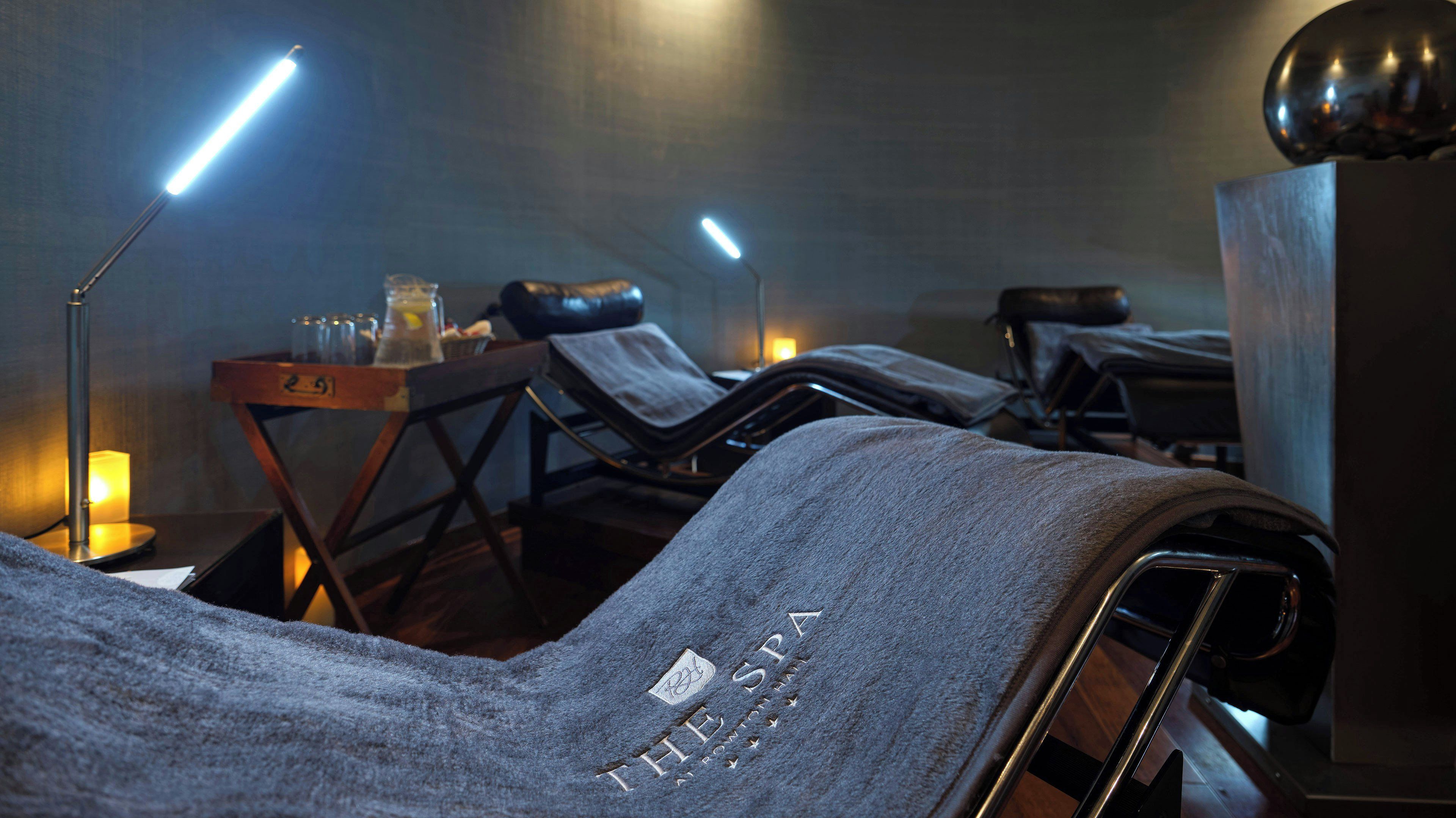 Un cuarto de spa con sillones reclinables, una camilla de masaje y dos lámparas de pie.