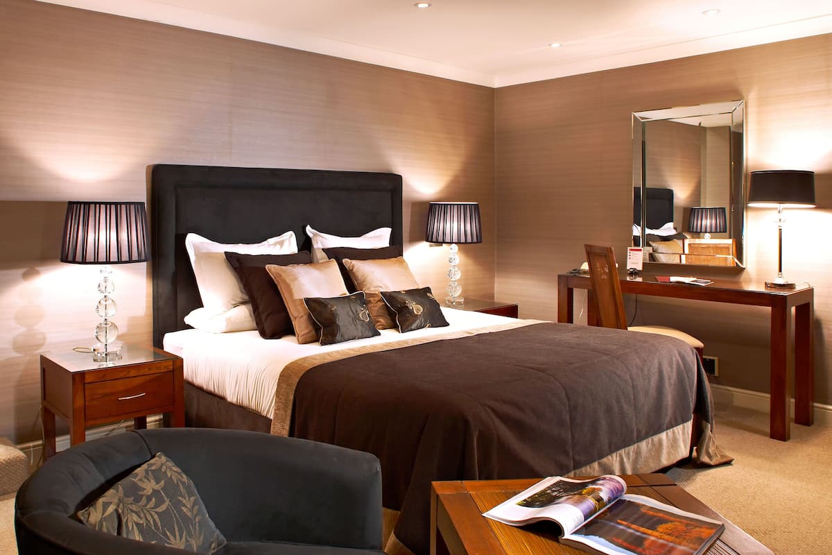 A hotel room with a large bed, bedside tables, a desk, a chair, and a mirror.