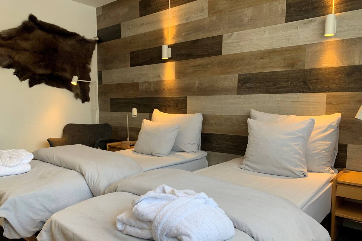 A hotel room with three beds, a fur headboard, and a wooden wall panel.