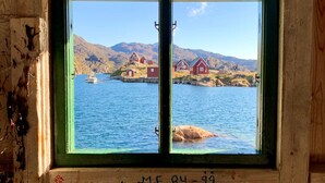 A wooden cabin with a window overlooking a fjord, featuring red houses and a boat. - Hotel Sisimiut (Sisimiut)