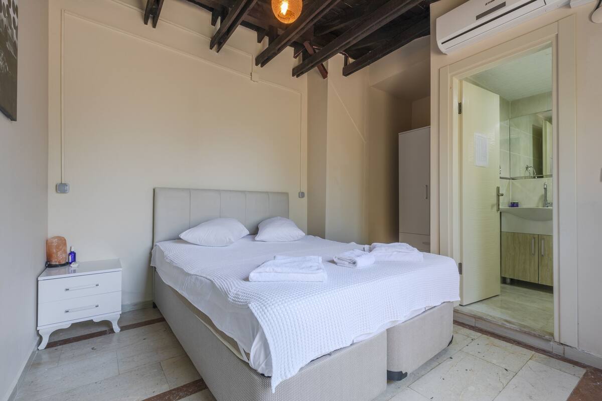 A bedroom with a bed, nightstand, and a bathroom visible through an open door.