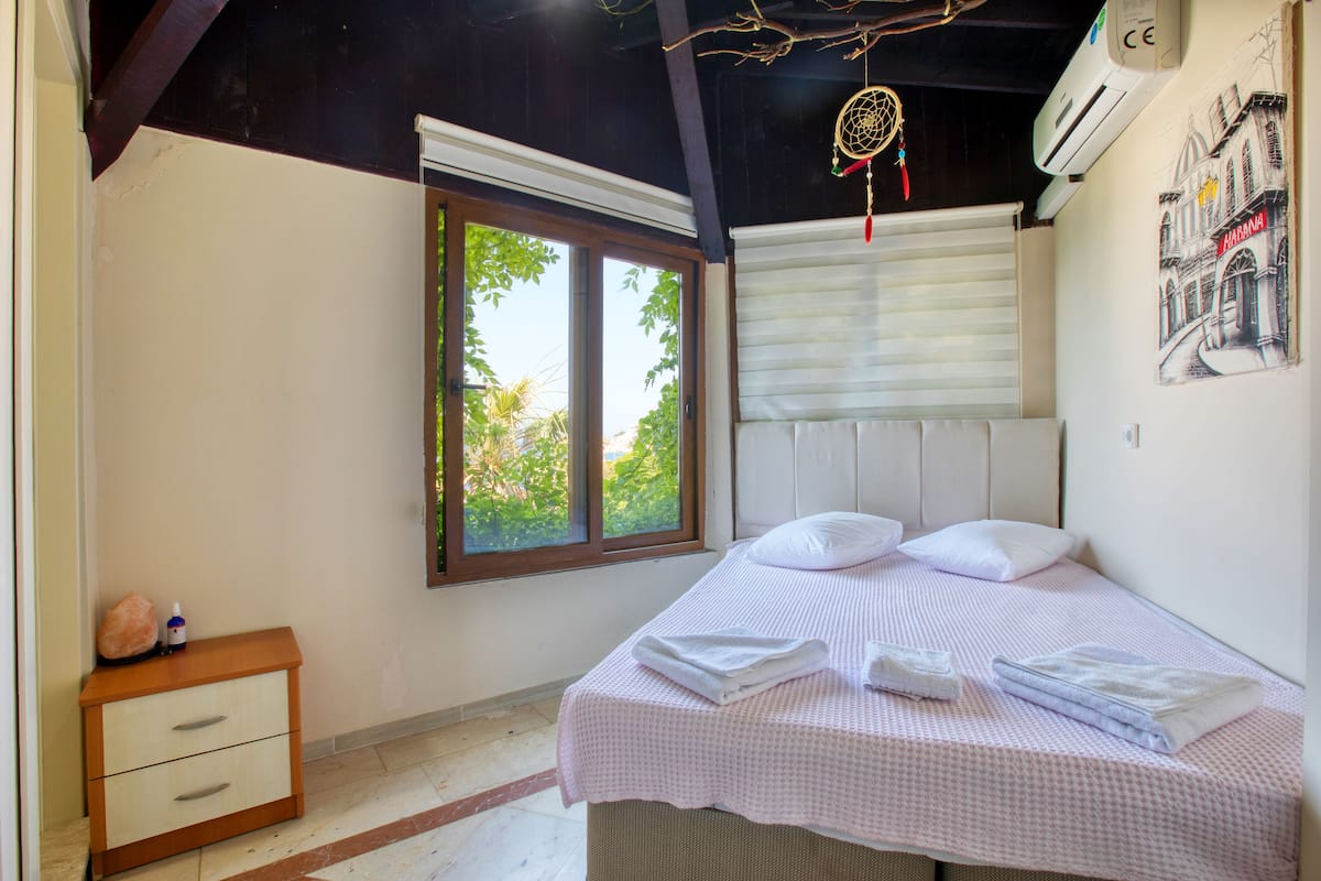 A bedroom with a bed, a nightstand, a window, and a wall-mounted air conditioner.