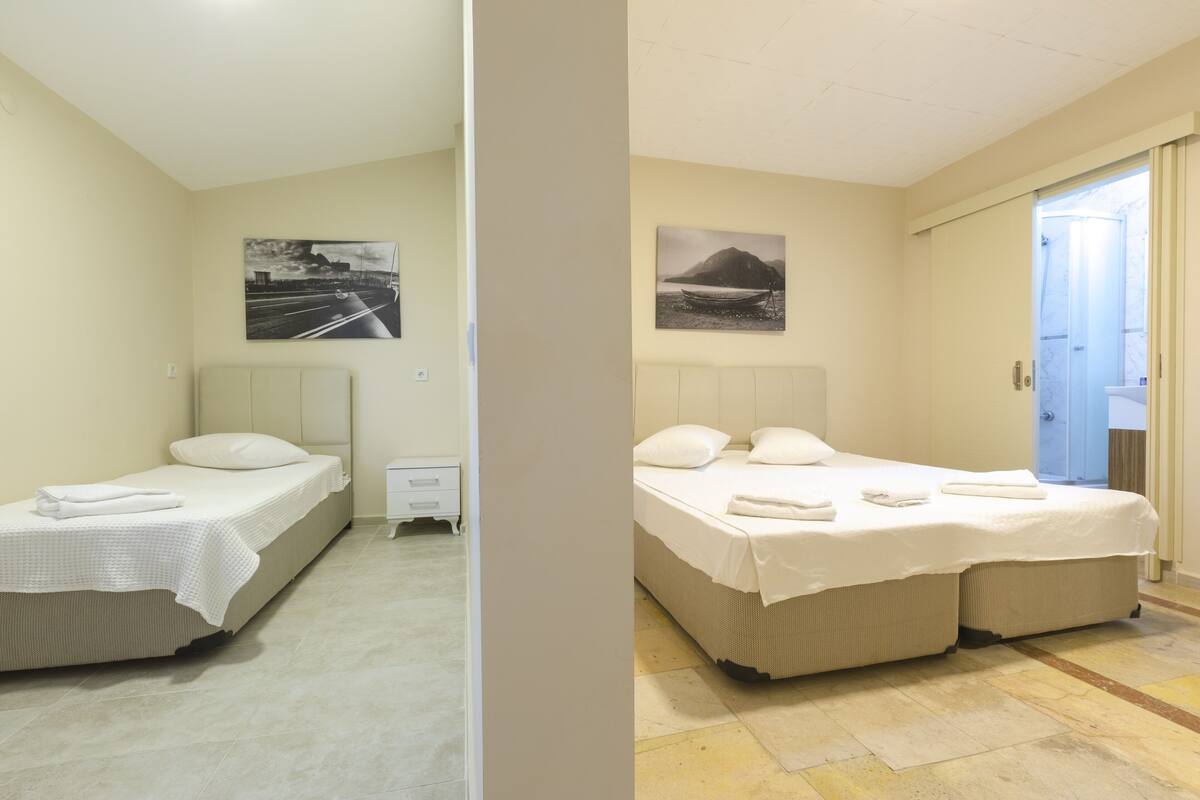 A hotel room with two beds, a small bedside table, a nightstand, and a wall-mounted painting.