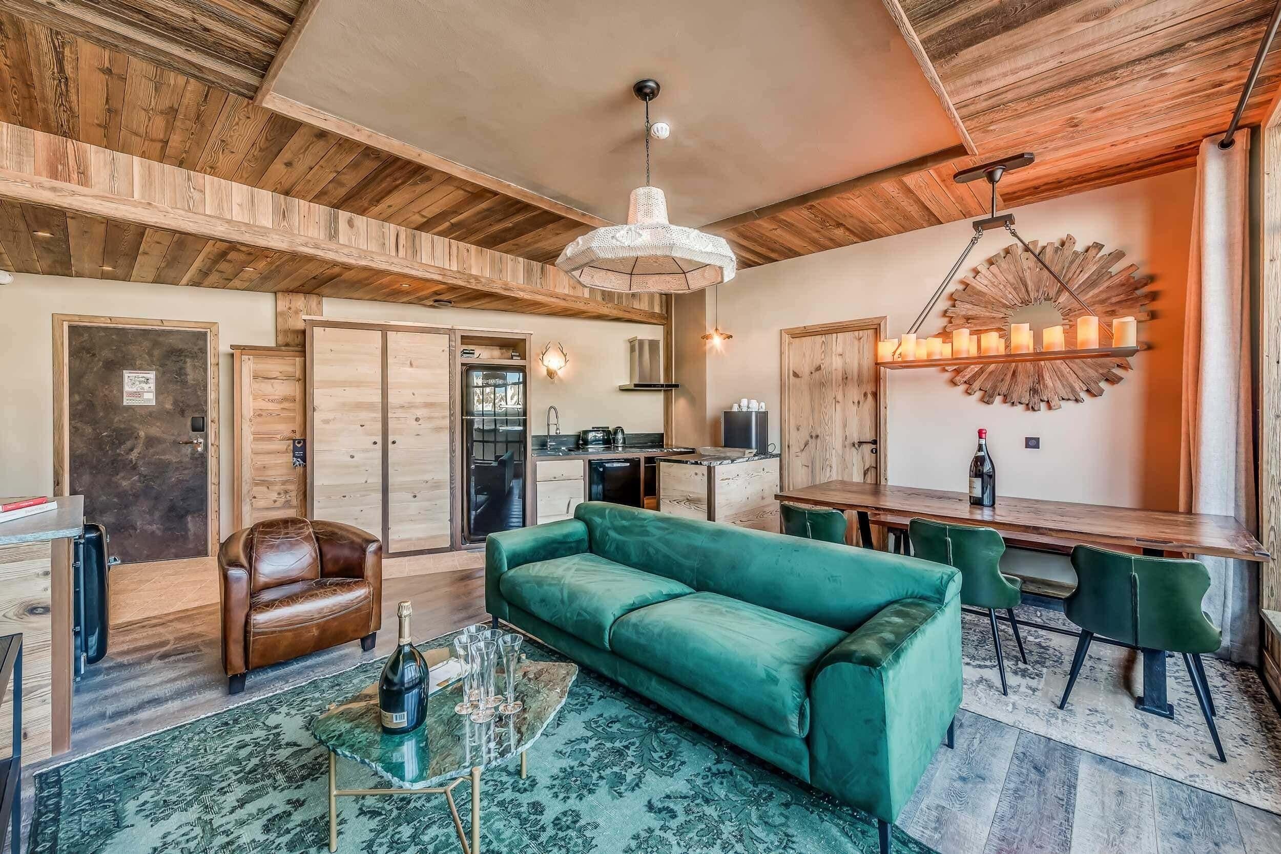 A cozy living room with a green sofa, a leather armchair, and a dining area with a wooden table and chairs.
