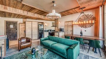 A cozy living room with a green sofa, a leather armchair, and a dining area with a wooden table and chairs.