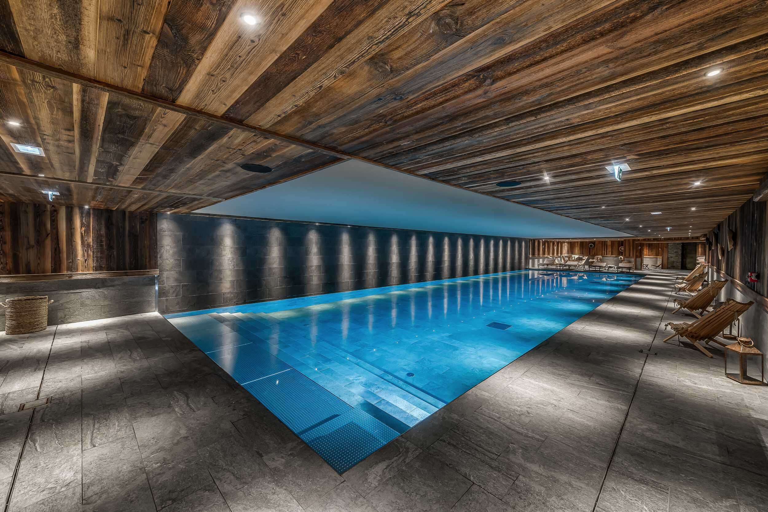 A spacious indoor swimming pool with a wooden ceiling and stone walls.