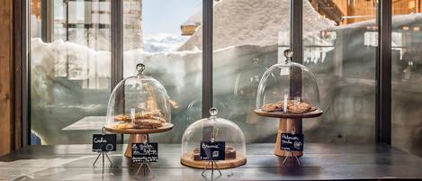Una exhibición de postres con tres artículos cubiertos en un escaparate, con una vista nevada de montañas al fondo.