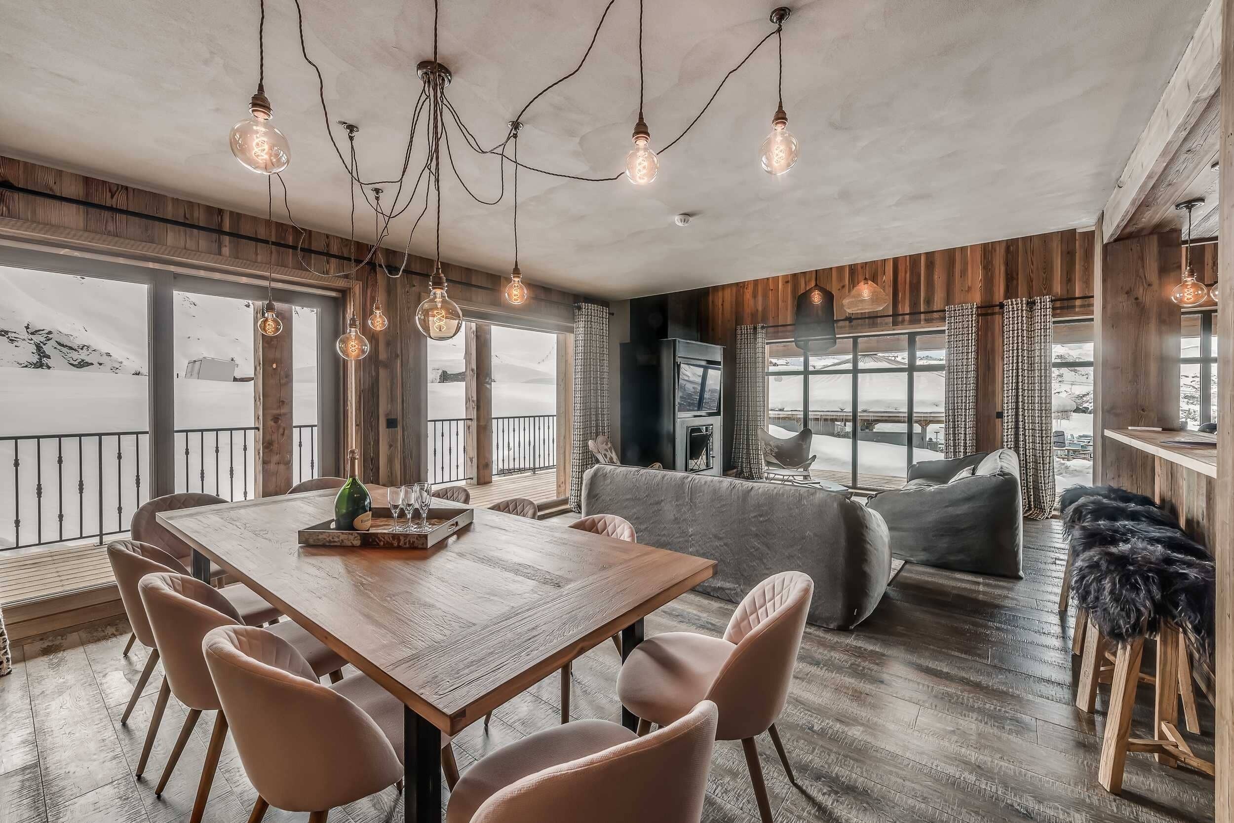 Un salón amplio con una mesa de comedor de madera, asientos cómodos y grandes ventanales con vistas al exterior.