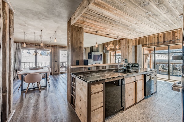 Una cocina rústica con una isla de madera, ventanas amplias y un comedor con mesa y sillas.