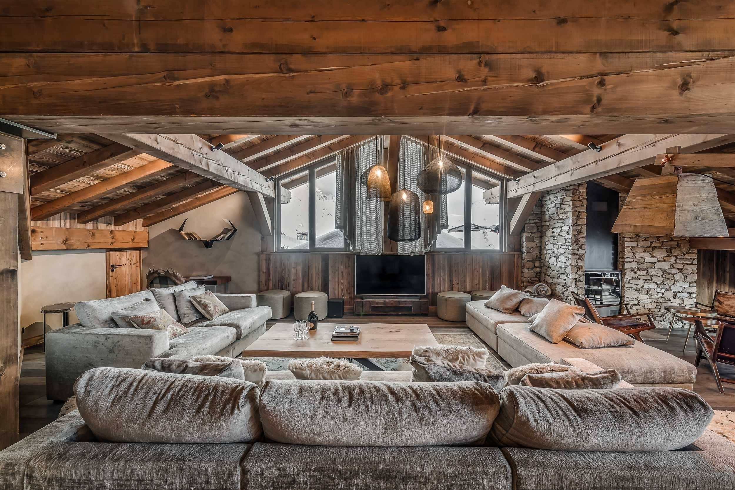 A cozy living room with a stone fireplace, wooden beams, and a large sectional sofa.