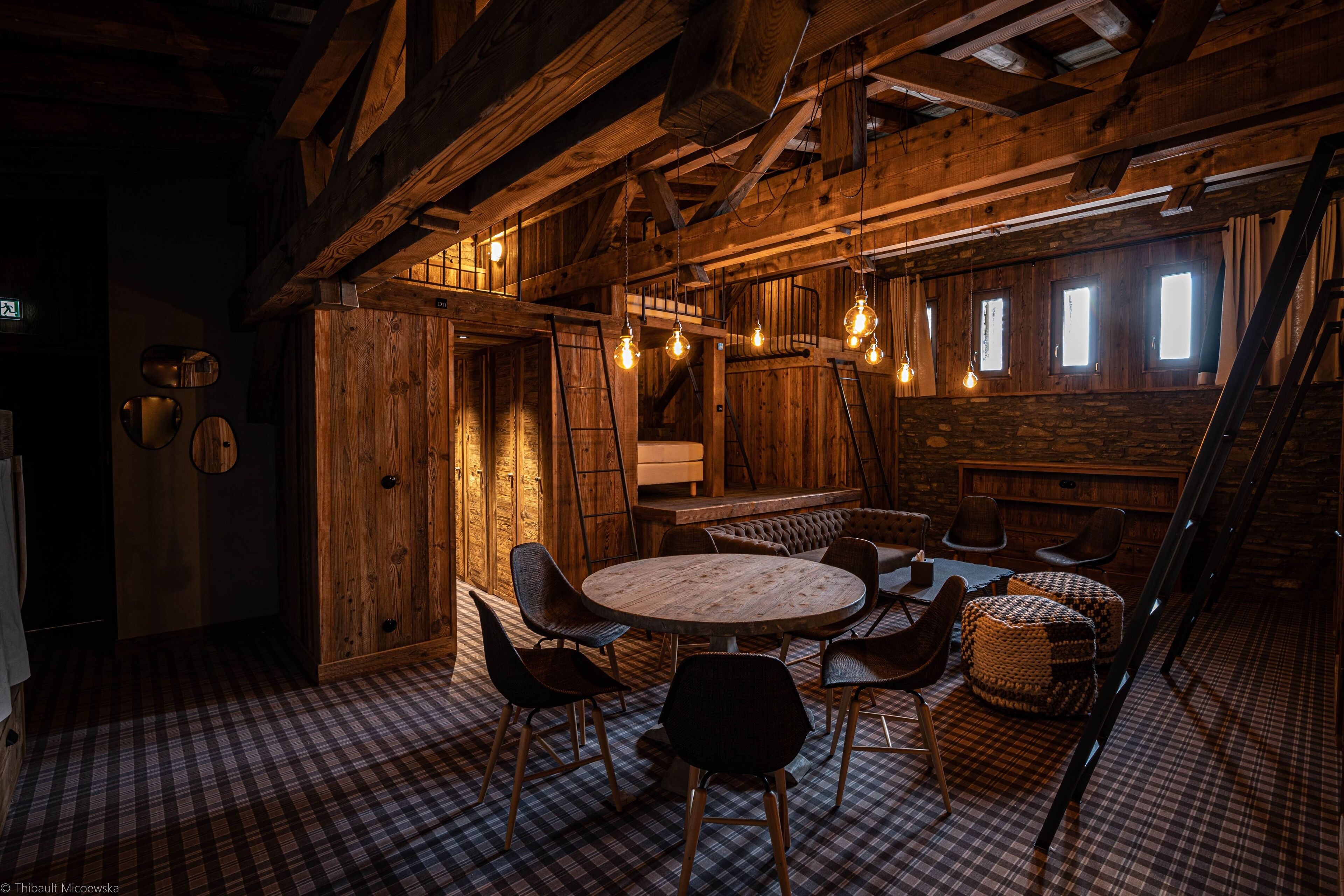 Ein rustikaler Holzraum mit einem runden Tisch, Stühlen, einer Treppe und einem Schachbrettmuster-Boden.