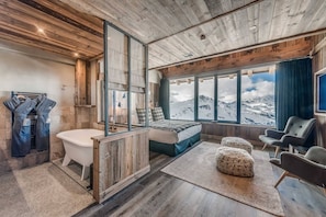 Un dormitorio moderno con un ventanal grande, techo de madera y vistas a montañas.