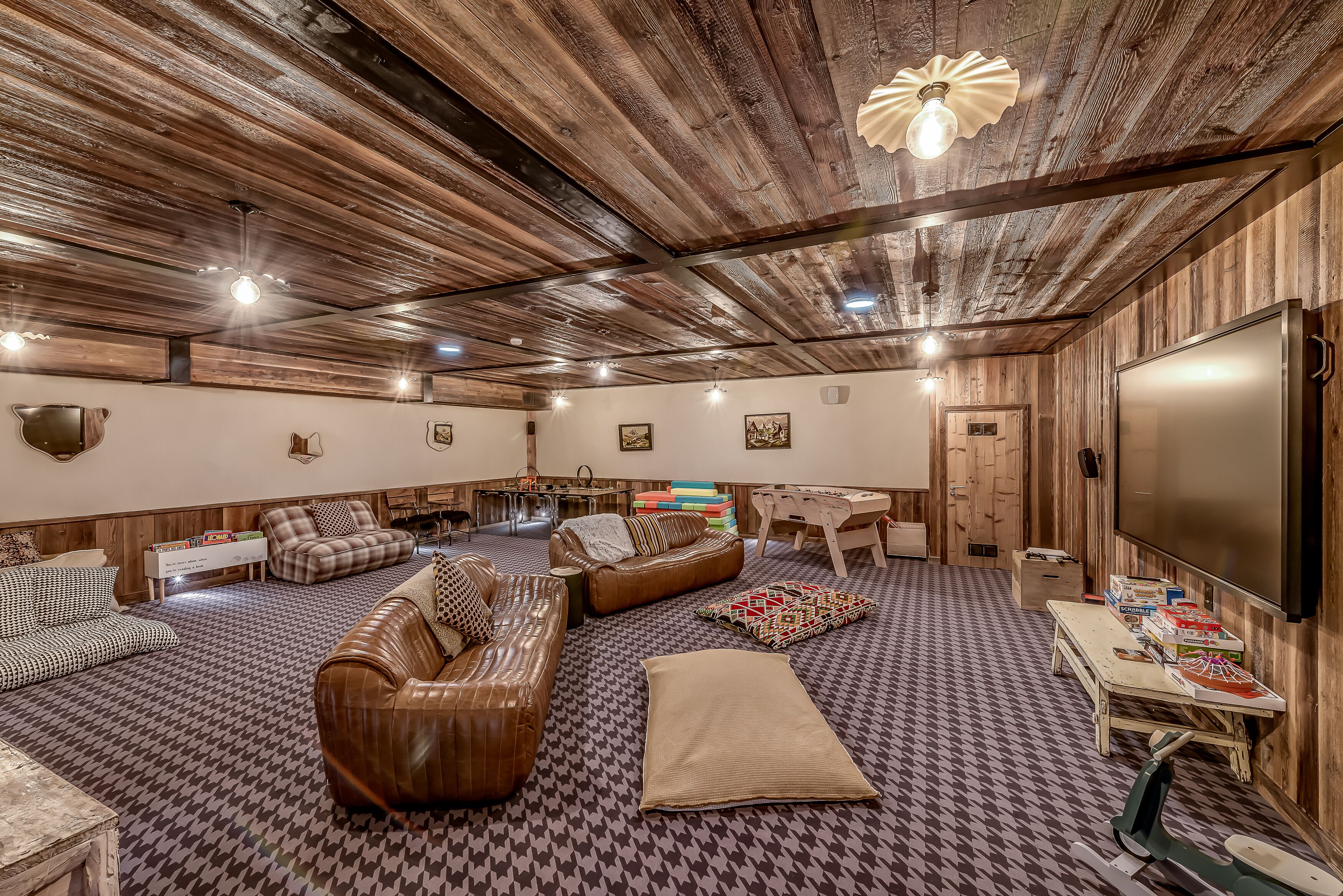 Un'ampia zona giorno con pavimento a spina di pesce, divani in pelle e soffitto in legno.
