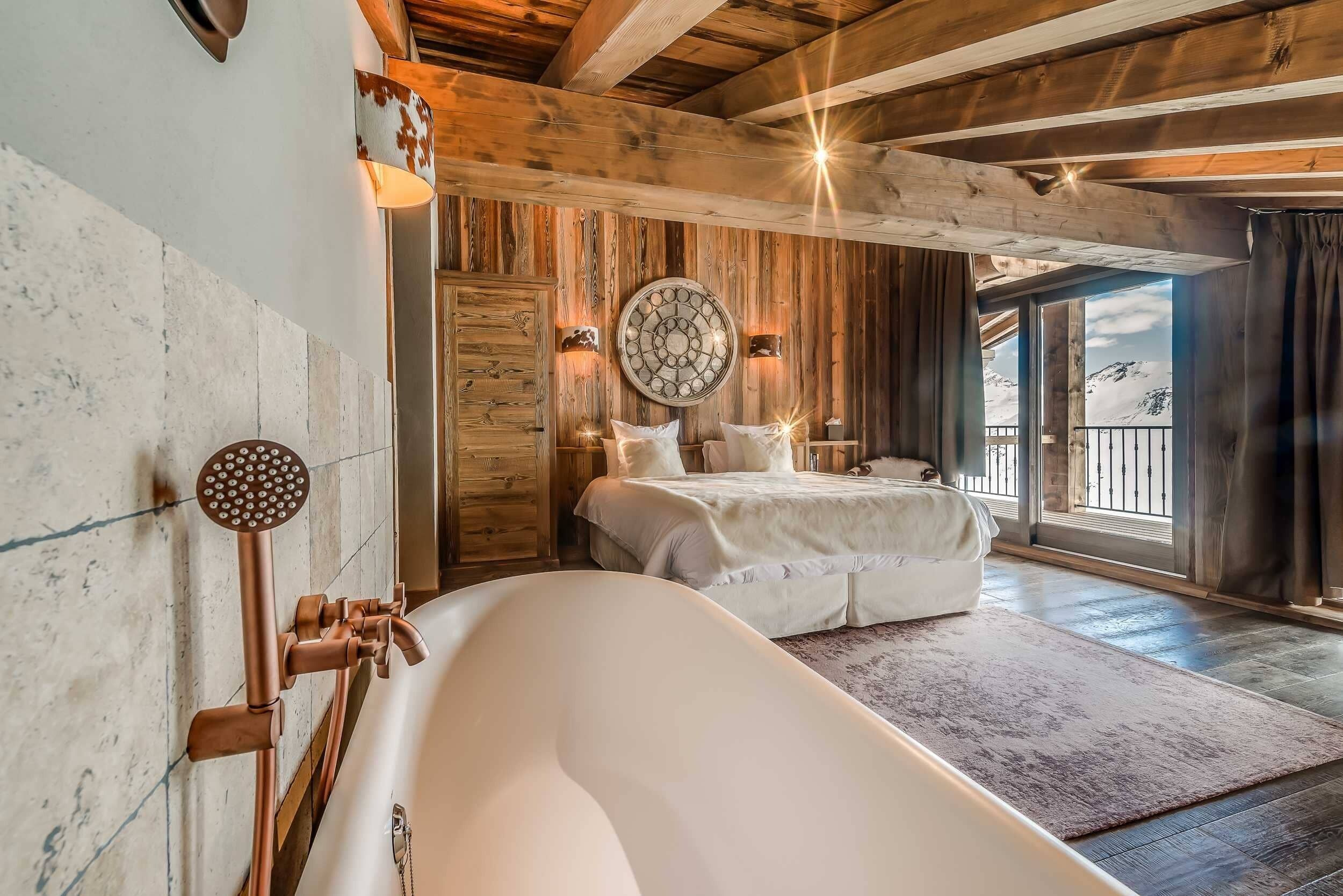 Une chambre spacieuse avec un grand lit, une baignoire, des murs en bois et une vue sur les montagnes.