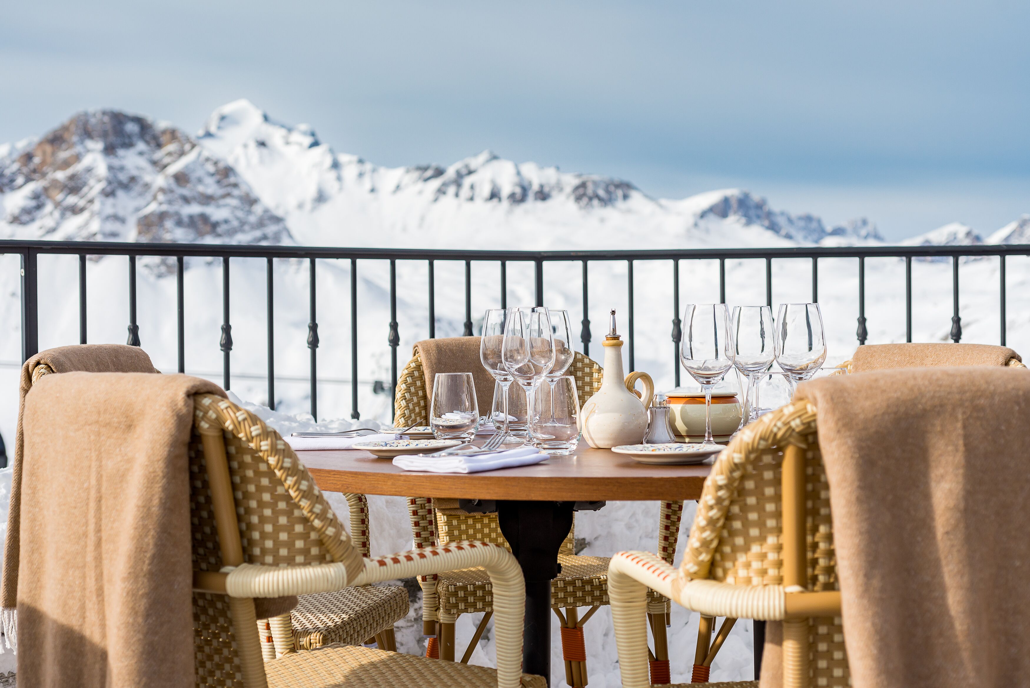 Une table à manger dressée avec des verres, des assiettes et un pichet, donnant sur des montagnes enneigées.