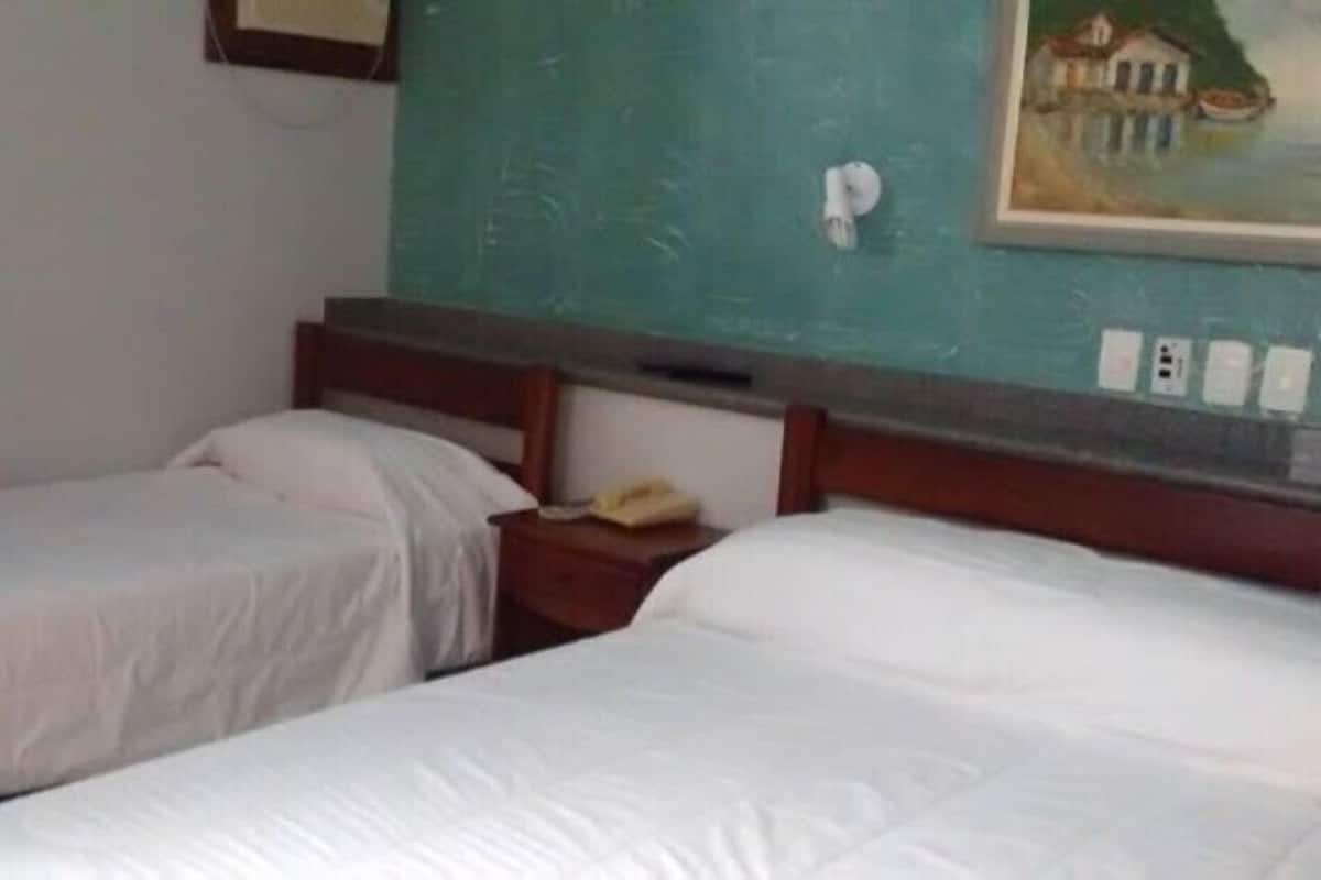 A hotel room with two single beds, a wooden headboard, a small bedside table with a telephone, and a painting on the wall.