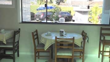 Un comedor con una mesa redonda y cuatro sillas, una ventana que ofrece vistas a coches estacionados y vegetación exterior.