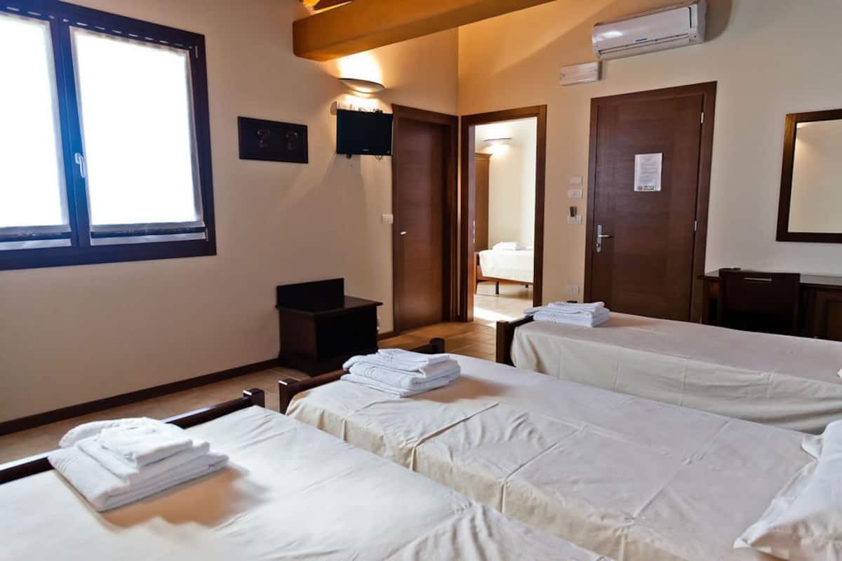 A hotel room with two beds, a television, an air conditioning unit, and a window with blinds.
