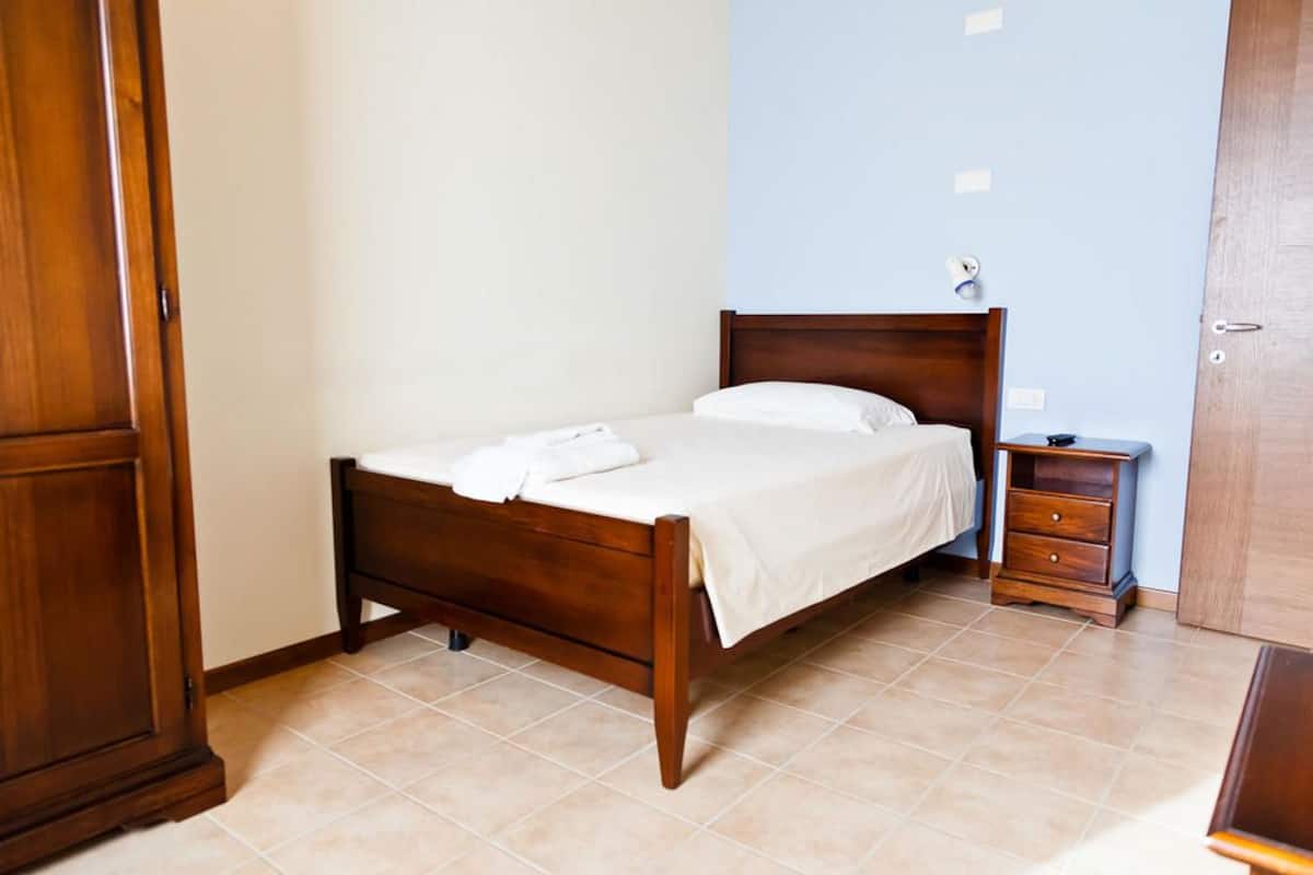 A neatly made bed with a wooden headboard in a room with tiled flooring and a blue accent wall.
