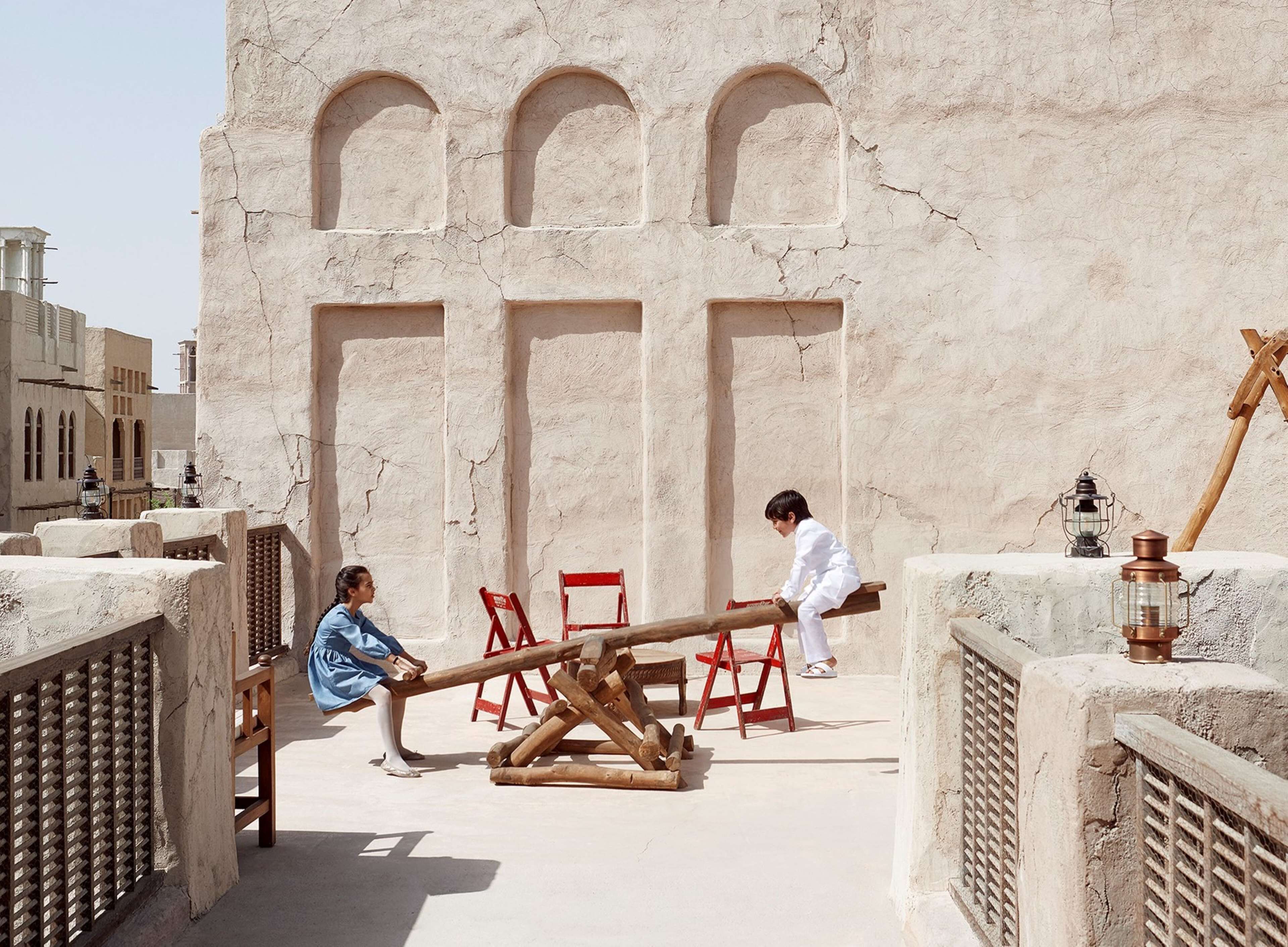 A courtyard with a seesaw, a wooden bench, and a red chair.