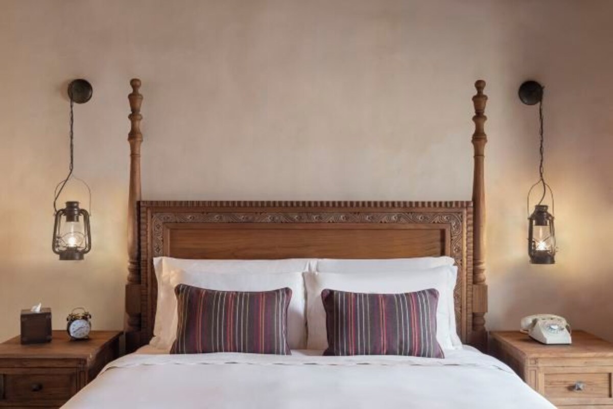 A four-poster bed with a wooden headboard, two bedside tables, and two wall-mounted lanterns.