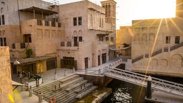 A narrow waterway flanked by buildings with multiple levels and balconies, a bridge crossing over the water, and a small dock area.