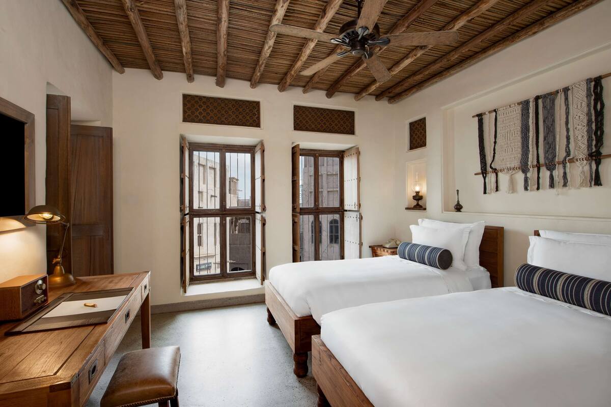 Une chambre avec deux lits, des meubles en bois, un bureau, une lampe et un ventilateur de plafond.