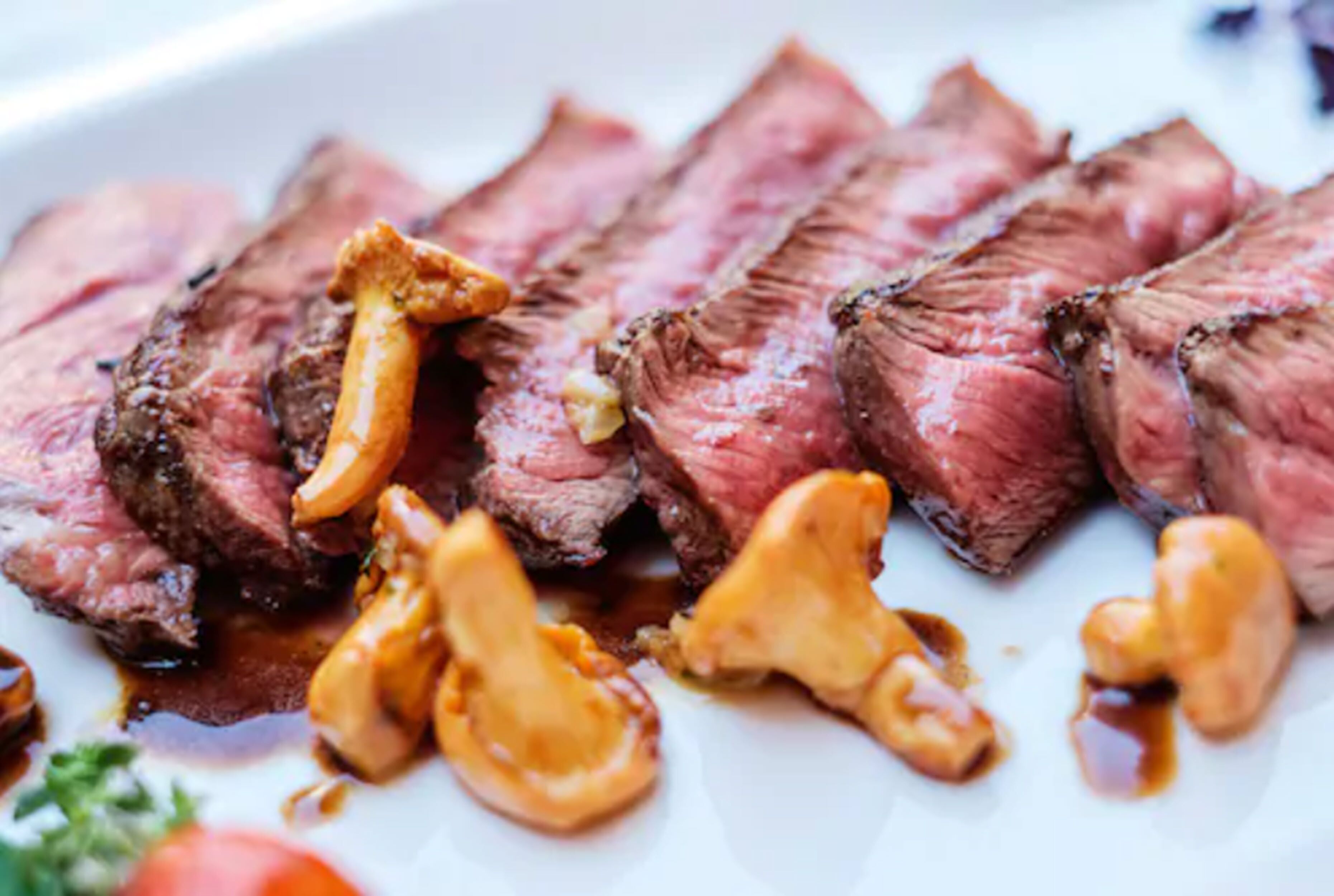 A plate of sliced steak with mushrooms and a garnish of parsley.