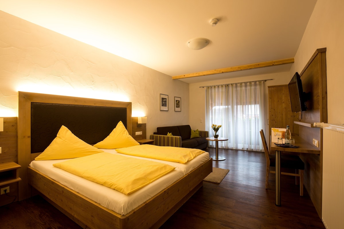 A hotel room with a wooden bed, a desk, a chair, a television, and a window with curtains.