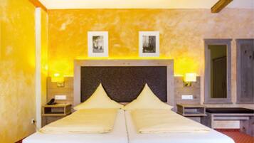Ein Hotelzimmer mit einem Doppelbett, zwei Nachttischen mit Lampen, einem großen Spiegel und zwei gerahmten Bildern an der Wand.