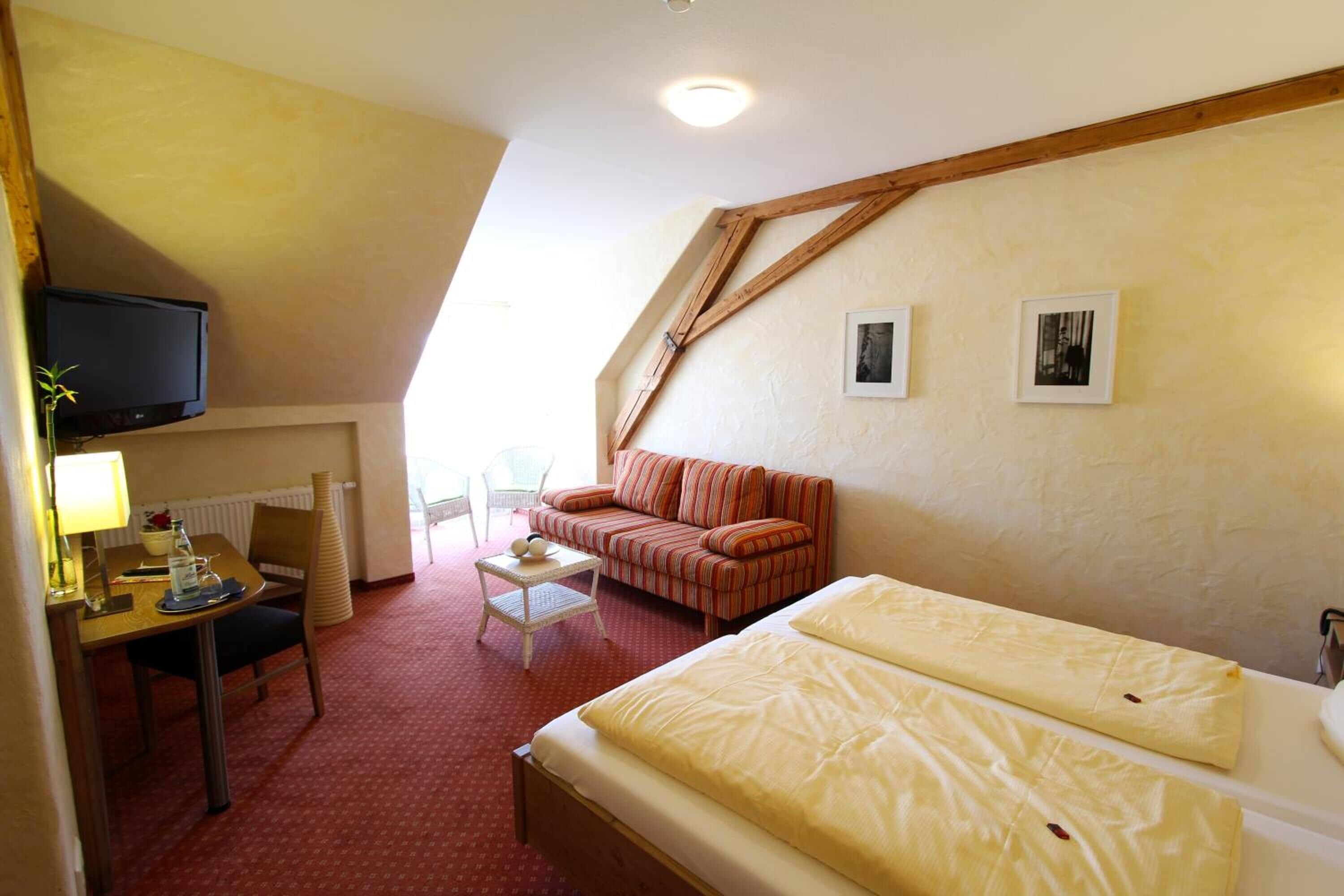 Une chambre d’hôtel comprenant un lit, un canapé, un bureau avec une chaise, une télévision et deux tableaux encadrés accrochés au mur.