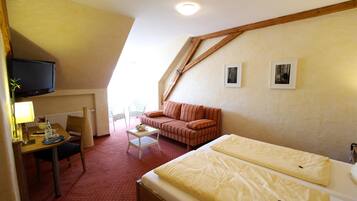 Une chambre d’hôtel comprenant un lit, un canapé, un bureau avec une chaise, une télévision et deux tableaux encadrés accrochés au mur.