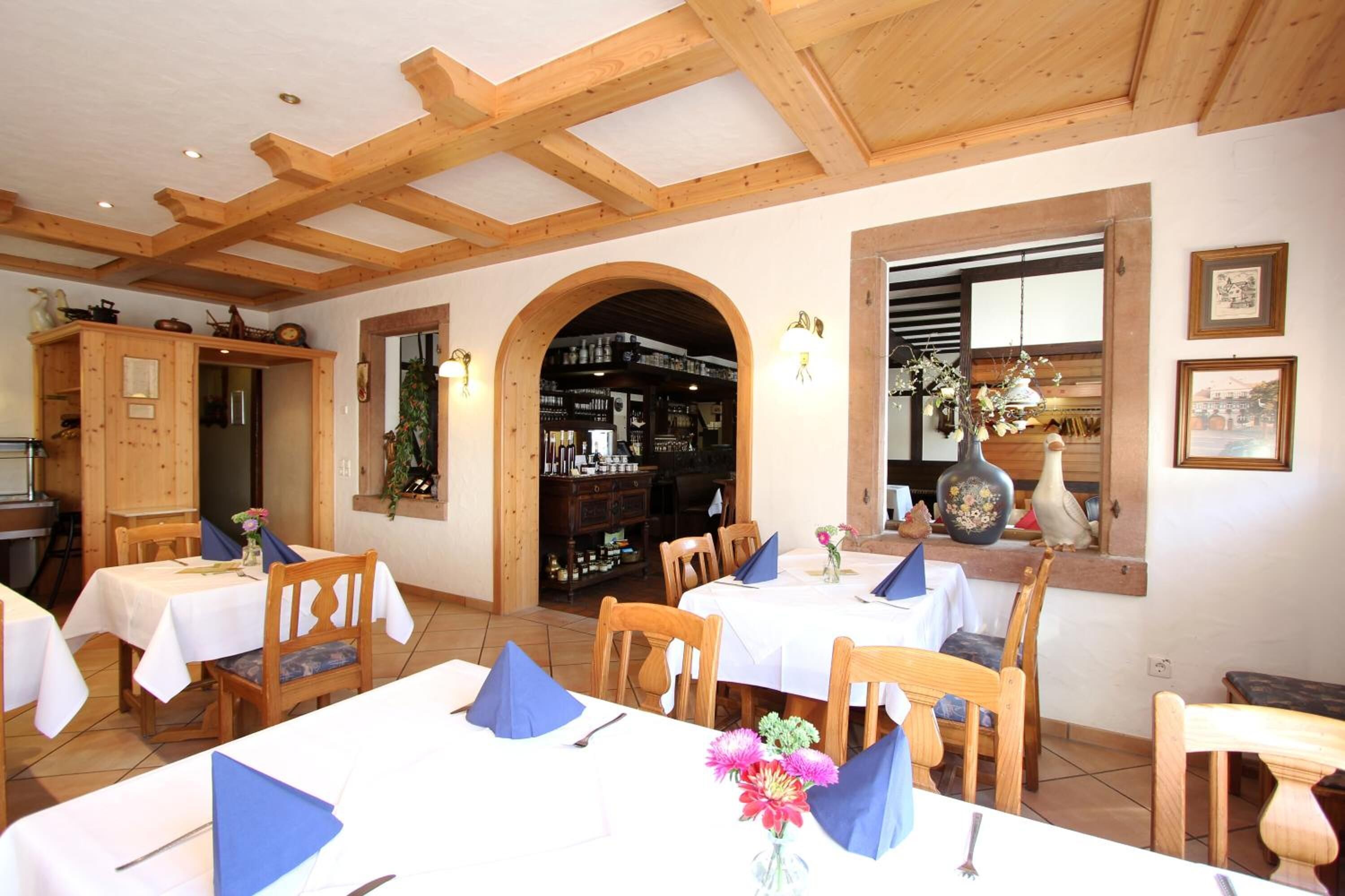 A restaurant with wooden beams, tables set with blue napkins, and a visible wine rack.