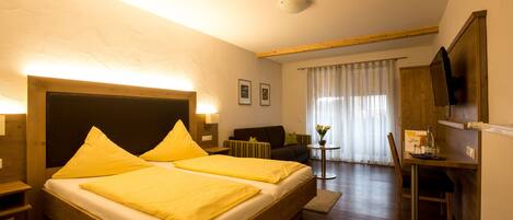 A hotel room with a wooden bed, a desk with a chair, a sofa, and a television.
